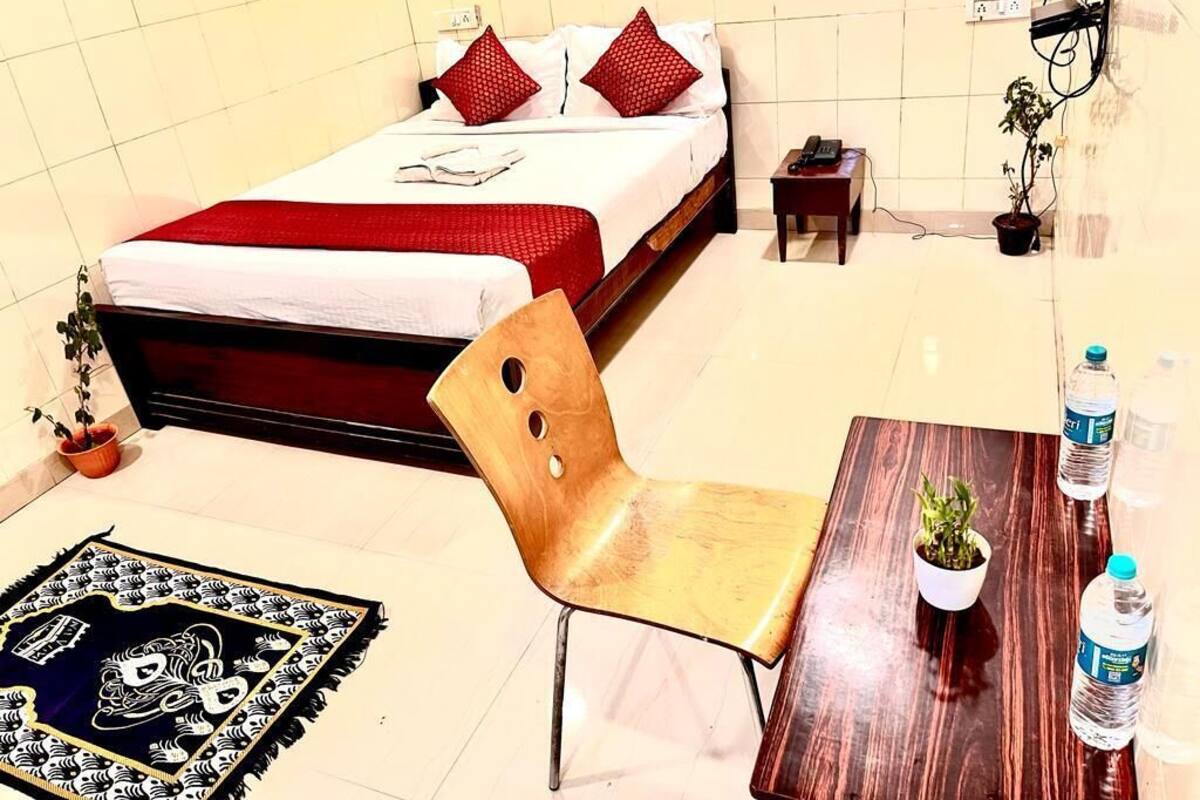 A hotel room with a bed, a wooden chair, a small table with a plant, and a water bottle.