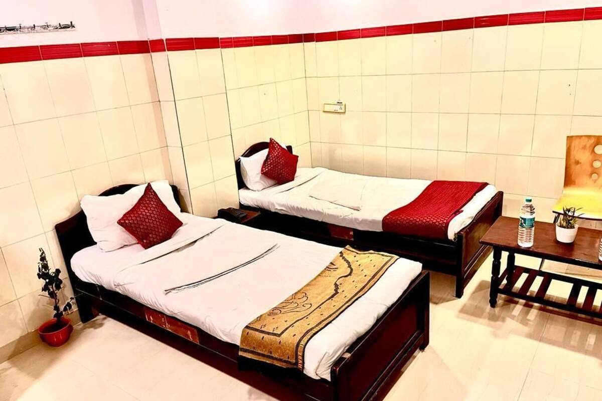 Two single beds with red and white bedding, a small wooden table with a bottle and a plant, and a tiled wall with a red border.
