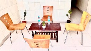 A dining area with a wooden table and four chairs, two on each side. There are two potted plants on the table, and two water bottles. - HOTEL SITA GRAND (Hyderabad)