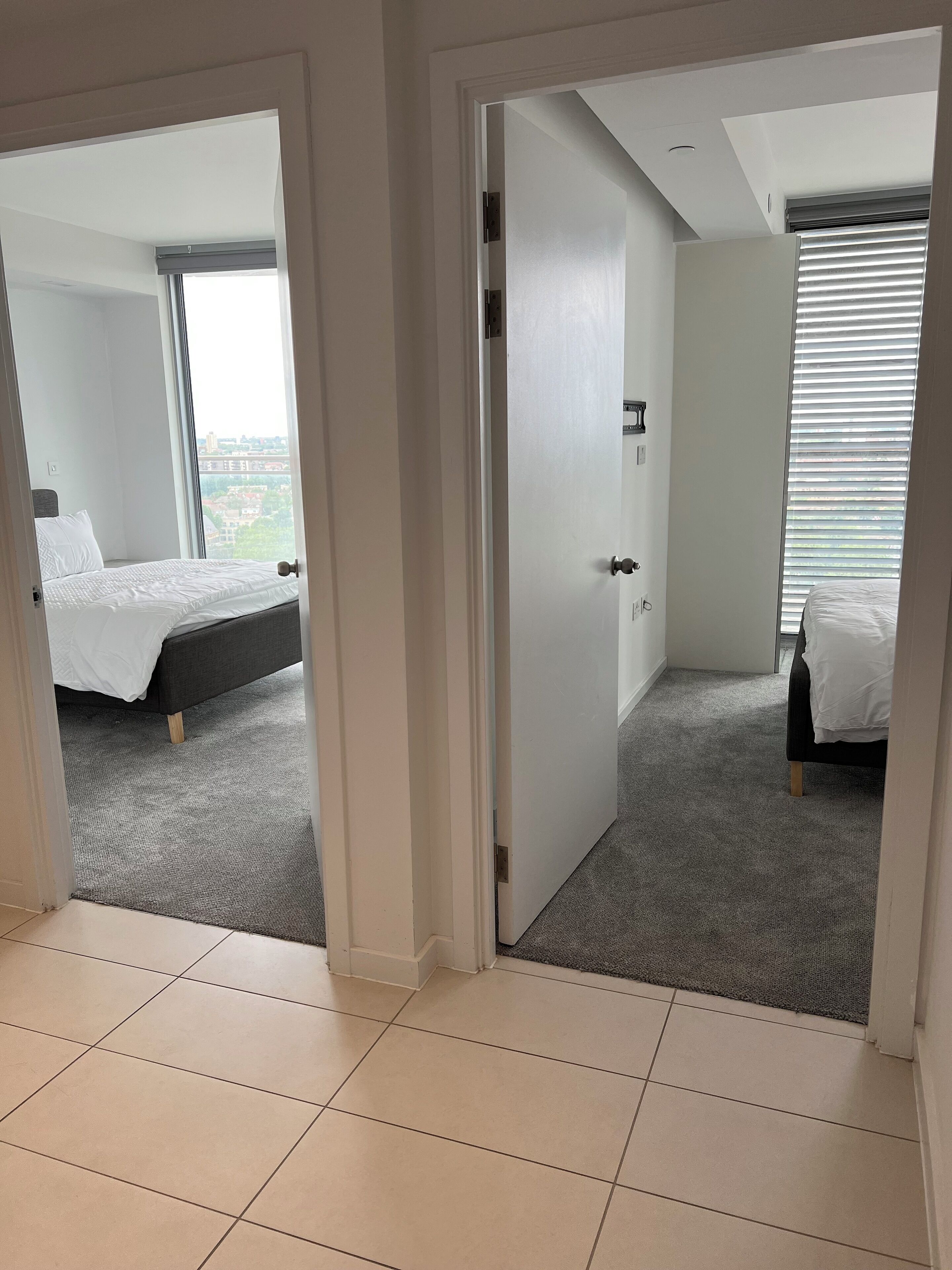 A hotel room with a bed, a window with blinds, and a view of the cityscape.