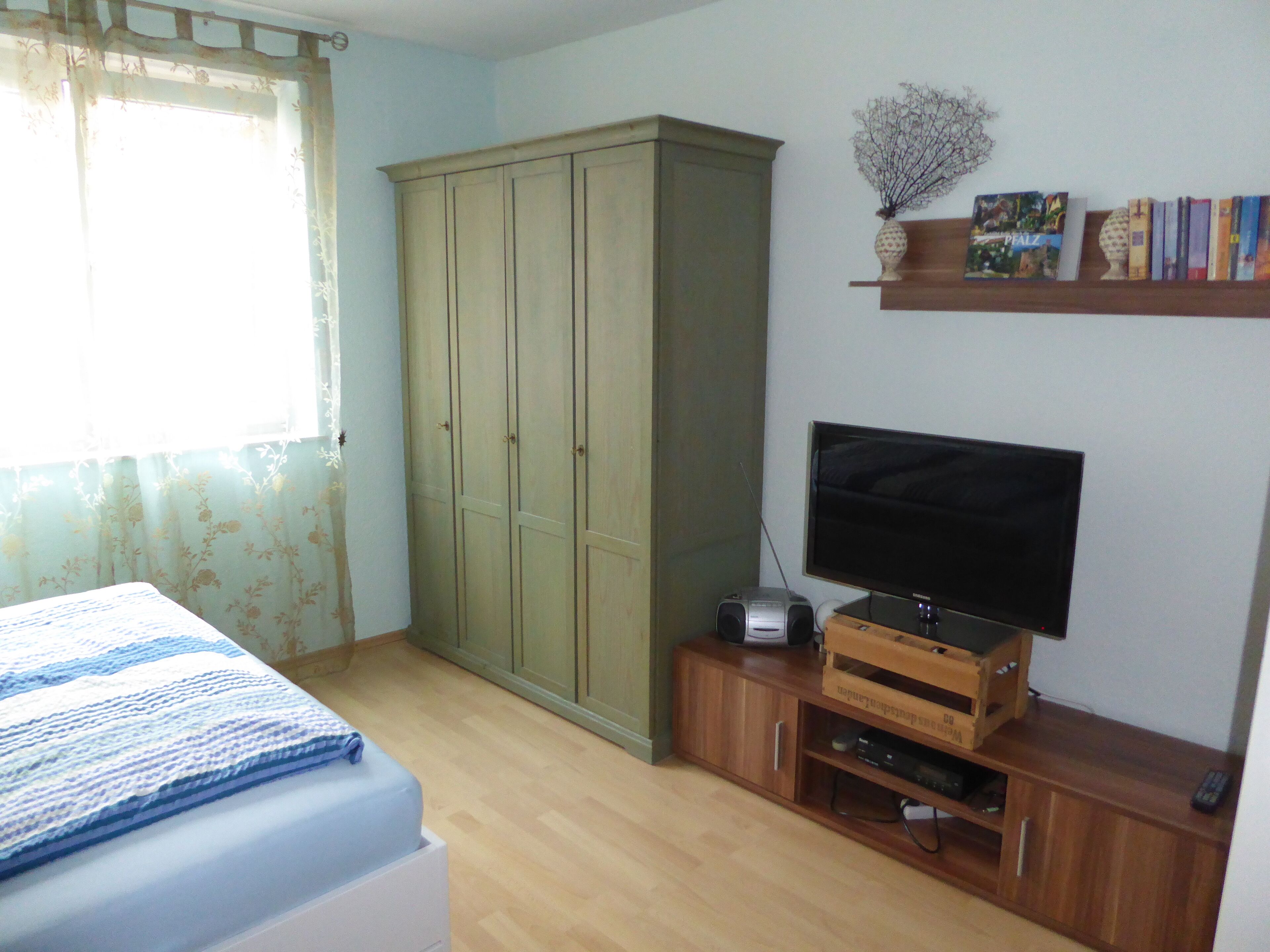 Ein Schlafzimmer mit Bett, Kleiderschrank, Fernseher und einem Bücherregal.