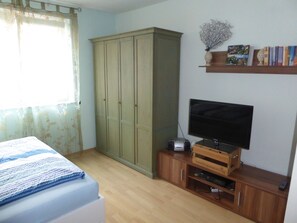Ein Schlafzimmer mit Bett, Kleiderschrank, Fernseher und einem Bücherregal.