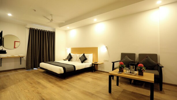 A hotel room with a bed, bedside table, lamp, and a small table with decorative items. - Hotel Golden World  (Ghaziabad)