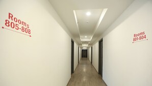 A long, narrow hallway with wooden flooring and white walls. There are directional signs on the walls indicating room numbers and corresponding phone numbers. - Hotel Golden World  (Ghaziabad)