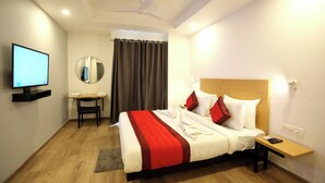A hotel room with a bed, bedside table, TV, and a small table with a chair. - Hotel Golden World  (Ghaziabad)