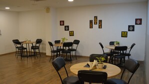 A conference room with multiple tables and chairs, some with plants. - Hotel Golden World  (Ghaziabad)