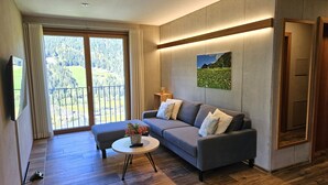 A modern living room with a grey sofa, a small round table with a vase, and a painting of a landscape on the wall.