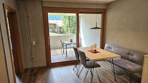 Un comedor con mesa, sillas, un banco y vistas a un balcón con mobiliario exterior.