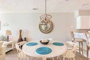 A dining area with a round table, chairs, a hanging light fixture, and a wall-mounted mirror.