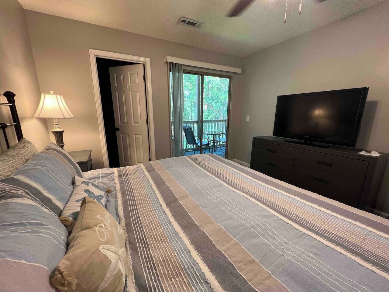 Een slaapkamer met een bed, een televisie, een dressoir en een glazen schuifdeur naar een balkon.