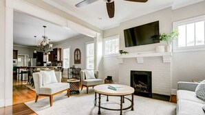 A spacious living room with a fireplace, a ceiling fan, and a television mounted above it. - Lovely Home & Guest Suite. Walk to City & Stadium. (Charlotte)