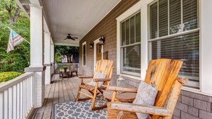 A wooden porch with two Adirondack chairs and a small table, a ceiling fan, and a patterned rug. - Lovely Home & Guest Suite. Walk to City & Stadium. (Charlotte)