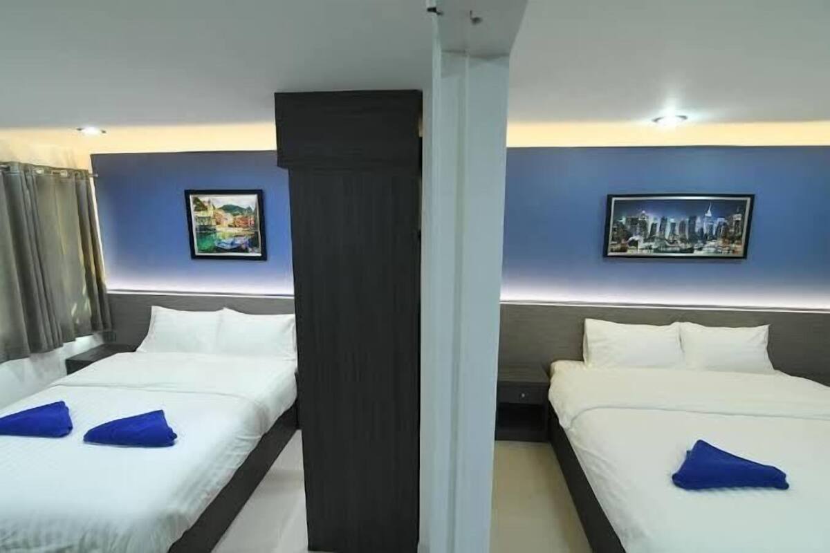A hotel room with two beds, each with white linens and blue towels. There are two framed pictures on the walls, one depicting a cityscape and the other a landscape.