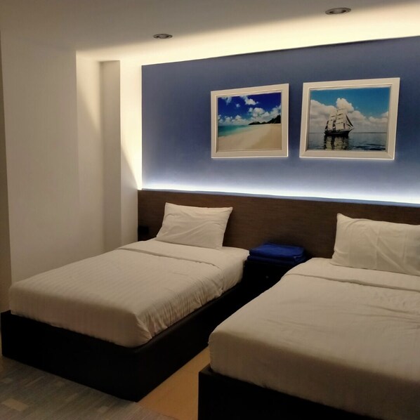 A hotel room with two beds, a headboard with built-in lighting, and two framed pictures on the wall.