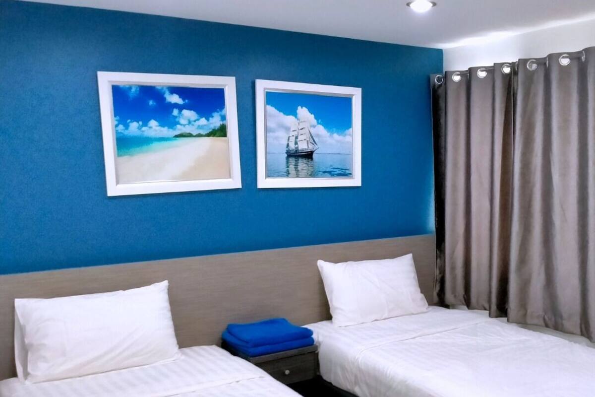 A hotel room with two beds, a blue wall, and two framed pictures of a beach and a sailboat.