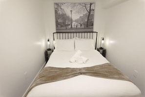 A neatly made bed with a white comforter and a brown throw blanket, flanked by two bedside lamps.