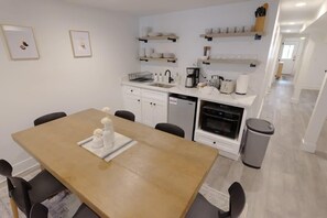 A modern kitchen with white cabinets, a wooden dining table, and a coffee machine.