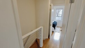 A narrow hallway with a wooden floor, a white door at the end, and a metal railing on the left. - Meridian Row | Sleeps 7 | Off St Parking! (Washington)