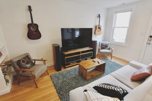 A living room with a TV, a guitar, a sofa, a chair, and a coffee table.