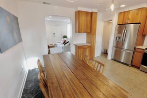 A modern kitchen with wooden cabinets, a stainless steel refrigerator, and a dining area with a wooden table and chairs.