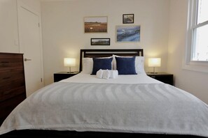 A neatly made bed with white and blue bedding, two bedside lamps, and three framed pictures on the wall. - Meridian Row | Sleeps 7 | Off St Parking! (Washington)