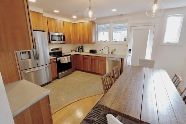 A modern kitchen with wooden cabinets, stainless steel appliances, a dining table, and a large window.