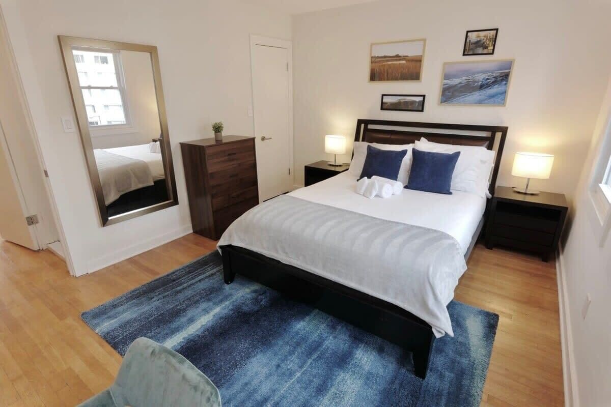 Ein Schlafzimmer mit einem Bett, Nachttischen, einer Kommode, einem Spiegel und Kunstwerken an den Wänden.