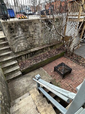 Eine Betontreppe führt zu einer Dachterrasse mit Feuerstelle und einem Baum.