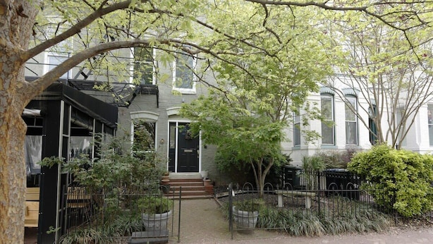 A residential building with a front entrance, a small porch, and a gated driveway.