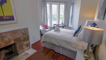 A bedroom with a fireplace, a bed with white bedding, a nightstand with a lamp, and a window with curtains.