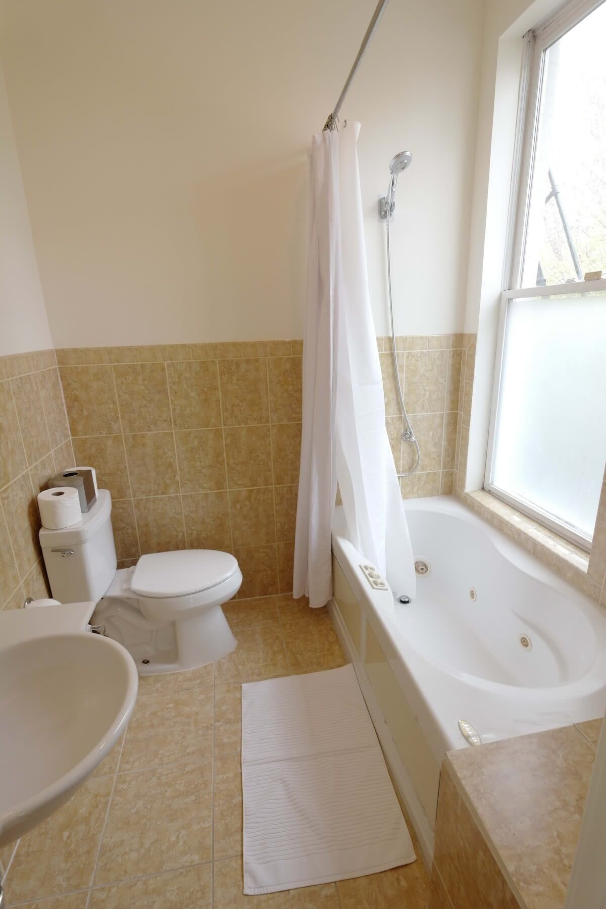 A bathroom with a toilet, bidet, bathtub, and a window.