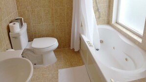 A bathroom with a toilet, bidet, bathtub, and a window.