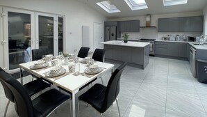 Eine moderne Küche mit einer zentralen Kochinsel, grauen Schränken und einem Essbereich mit einem weißen Tisch und schwarzen Stühlen.