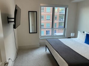 A bedroom with a bed, a window, a wall-mounted TV, and a door. - Preston Royal Double II I Premium 2BR in Dallas (Dallas)