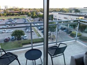 A balcony with a view of a parking lot and buildings. There are two chairs and a small table. - Preston Royal Double II I Premium 2BR in Dallas (Dallas)