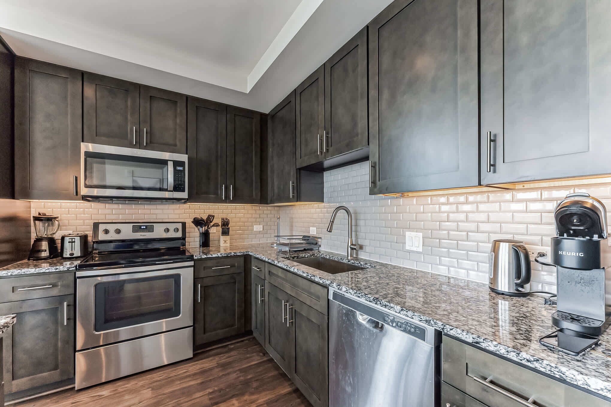 A modern kitchen with dark cabinets, stainless steel appliances, and a tiled backsplash.