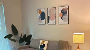 Ein Wohnzimmer mit einer Couch, einem blauen Sessel, einem Couchtisch und einer Lampe. An der Wand befinden sich abstrakte Gemälde.