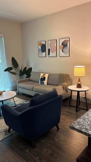 A living room with a sofa, a blue armchair, a coffee table, and a lamp. There are abstract paintings on the wall. - Preston Royal Single I Premium 1BR in Dallas (Dallas)