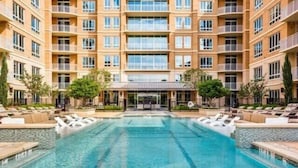 Ein mehrstöckiges Hotel mit einem zentral gelegenen Schwimmbecken, Außenbereich zum Sitzen und einem überdachten Eingang.