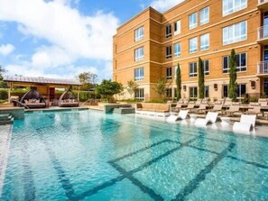 A hotel with a large outdoor swimming pool, lounge chairs, and a covered seating area.