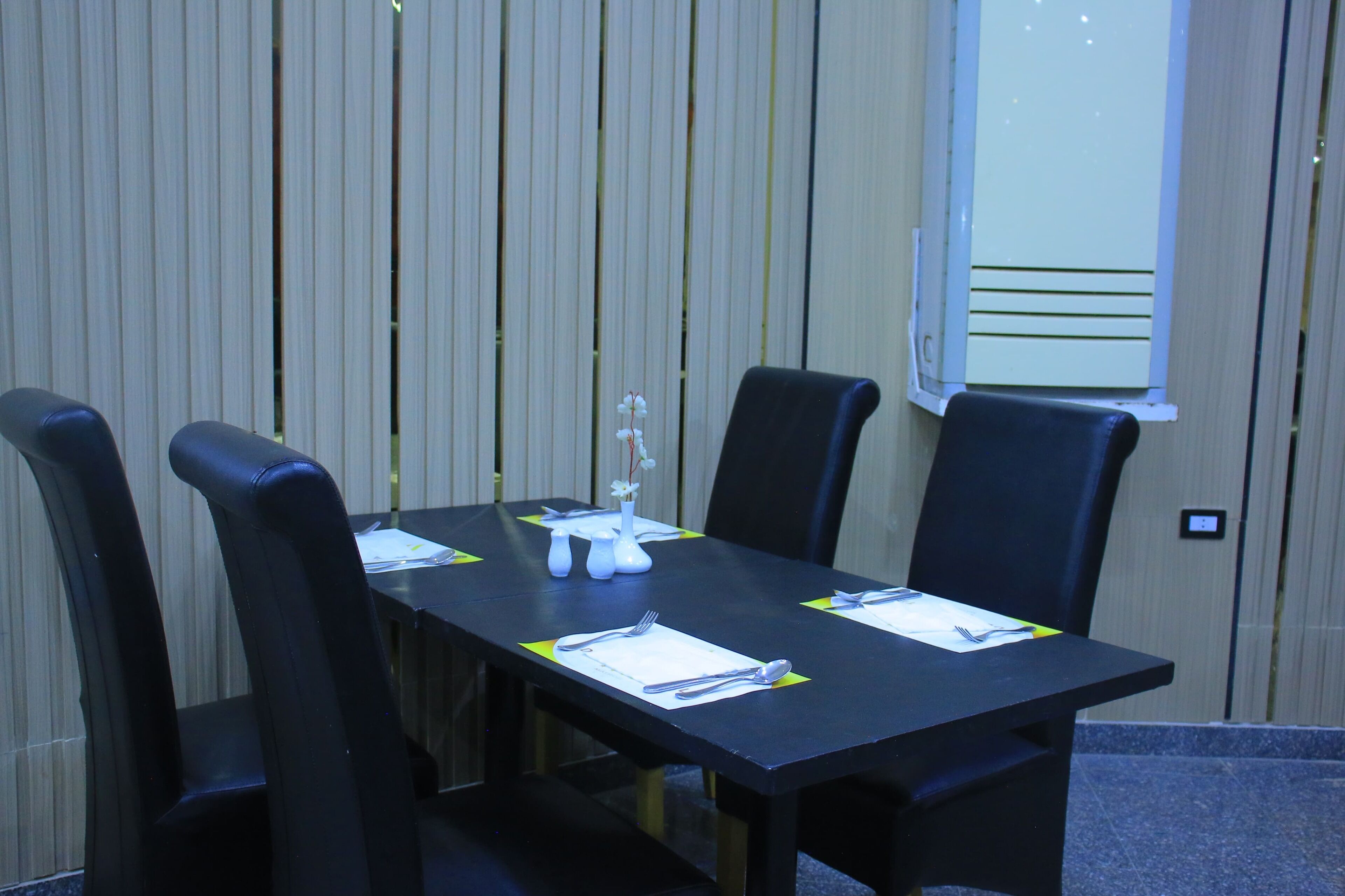 A conference room with a long table, four black chairs, and a projector screen.