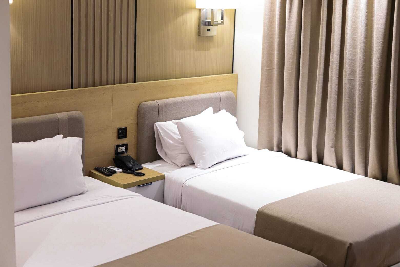 A hotel room with two beds, a bedside phone, and a light fixture on the wall.