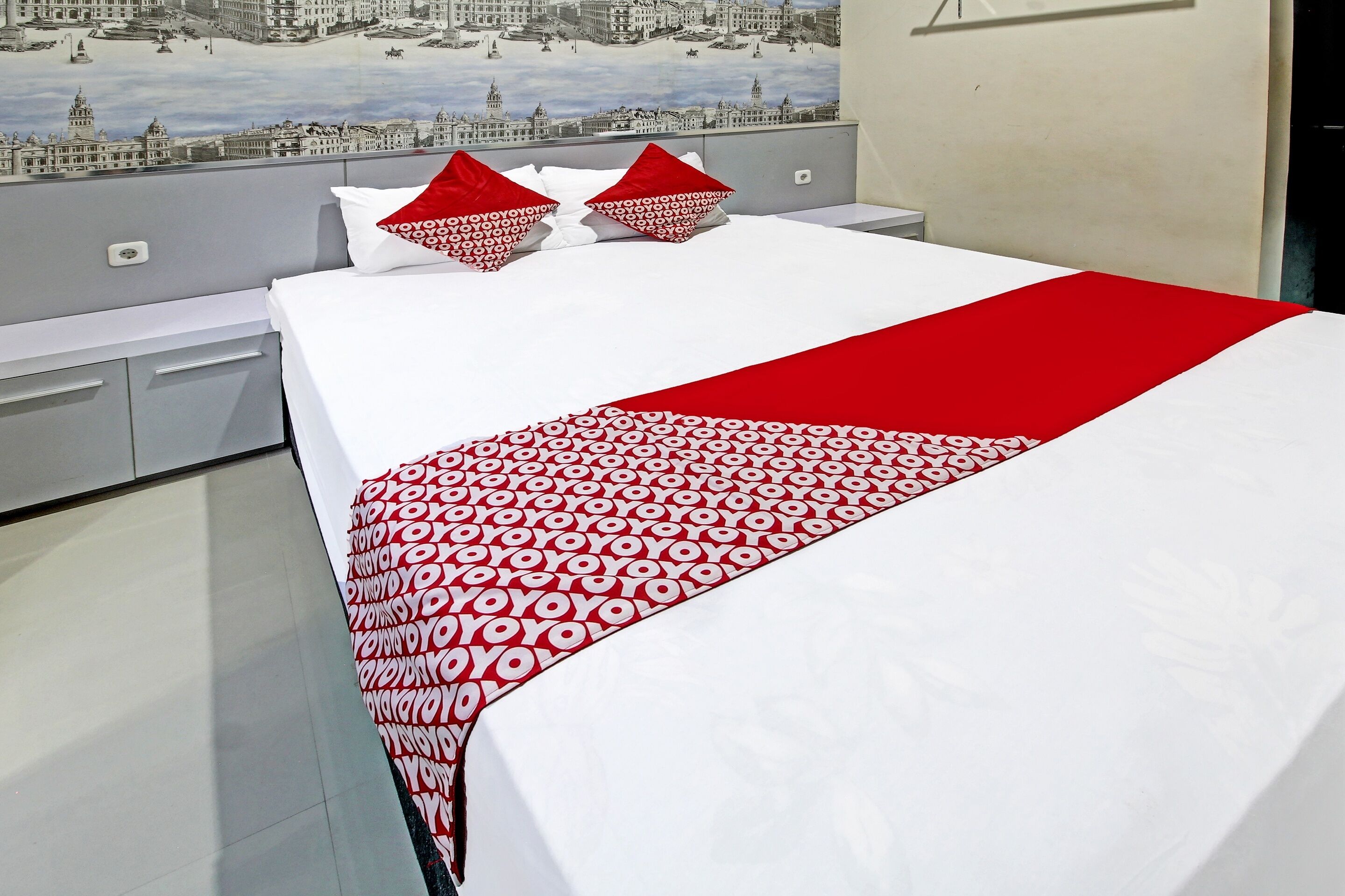Hotelkamer met een bed, een stadsgezicht muurschildering en een rode en witte gebloemde plaid.
