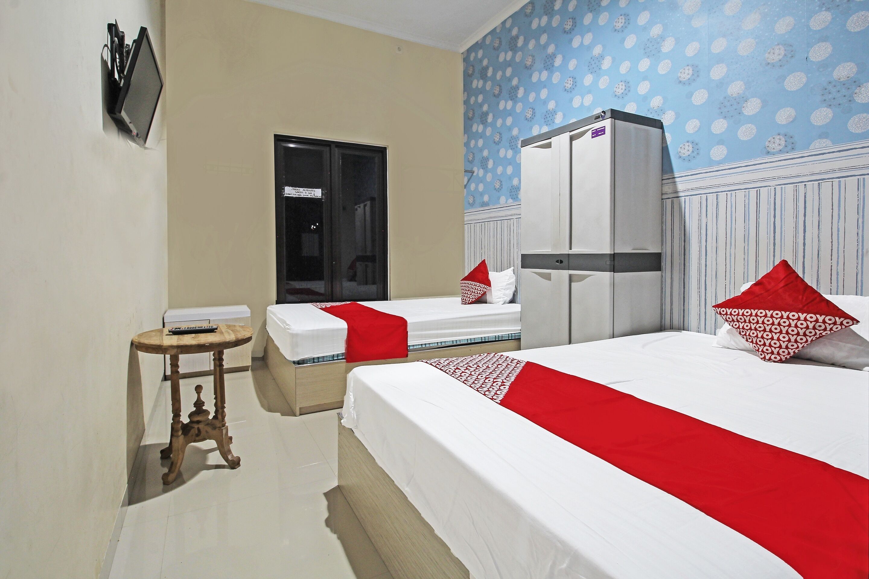 A hotel room with two beds, a wardrobe, a small table, and a television on the wall.