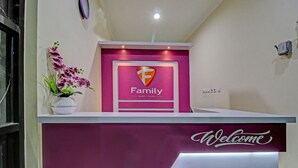Un mostrador de recepción con el logotipo 'Family' y un cartel de 'Bienvenido', una orquídea en maceta y una lámpara fijada a la pared.