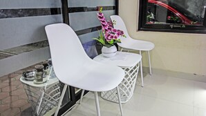 Una habitación moderna con dos sillas blancas, una mesita con un florero y una ventana que refleja un coche.