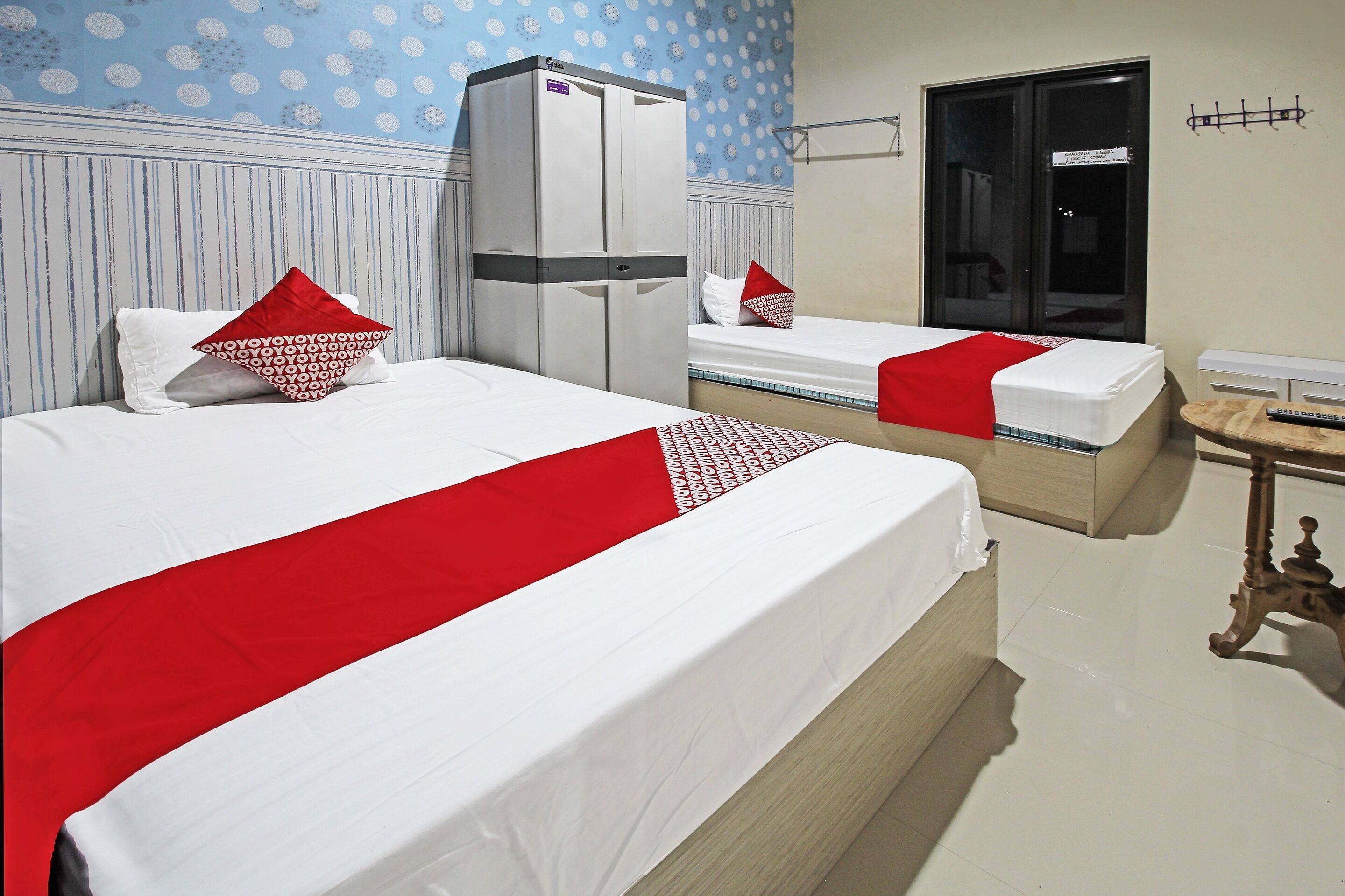 A hotel room with two beds, a wardrobe, a small table, and a door.