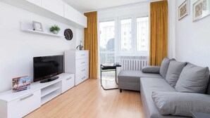 Ett modernt vardagsrum med en platt-TV, ett vitt förvaringsskåp, en grå soffa och ett fönster med gula gardiner.