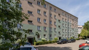 En flervåningsbyggnad med bostäder, som har en enhetlig fasad, flera fönster och en parkeringsplats med bilar.