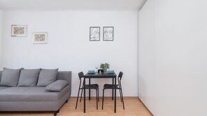Ett modernt vardagsrum med en grå soffa, ett litet matbord med två stolar och två inramade konstverk på väggen.
